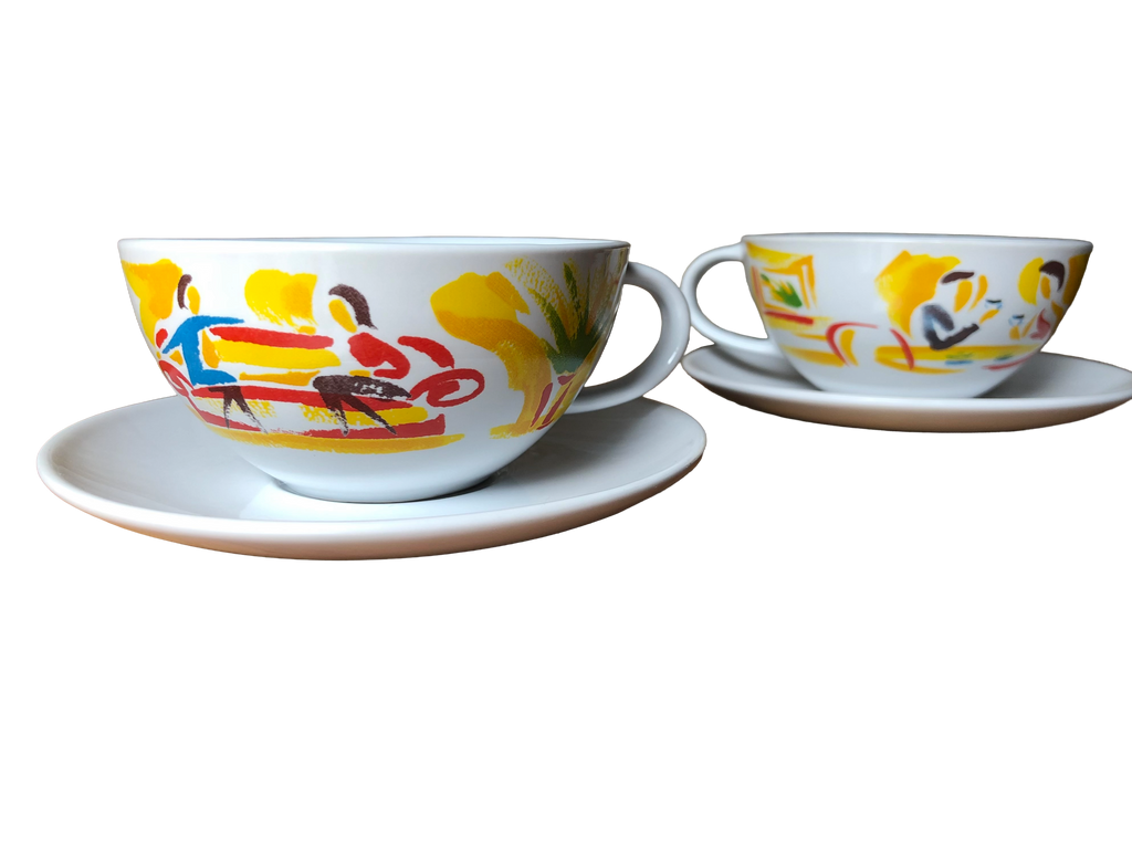 Photo of both cups on their saucers (front view): Pair of vintage Nescafé promotional coffee cups and saucers with brightly painted café scenes, UK, c.1988–92