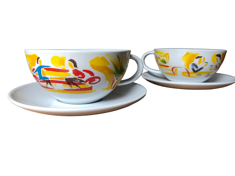 Photo of both cups on their saucers (front view): Pair of vintage Nescafé promotional coffee cups and saucers with brightly painted café scenes, UK, c.1988–92