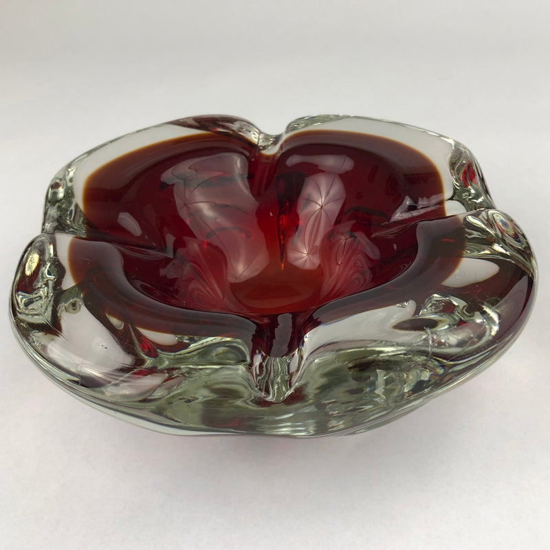 Three-quarter view of a vintage Murano sommerso cigar ashtray with a ruby-red interior and rounded clear glass rim.