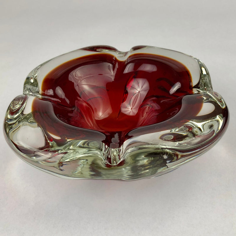 Vintage Murano glass cigar ashtray with a deep ruby-red bowl encased in thick clear glass, viewed at an angle.