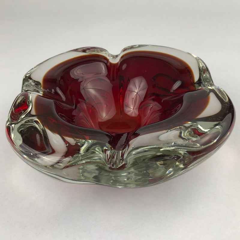 Ruby-red Murano glass cigar ashtray viewed from the front, showing a broad cigar rest and thick clear glass casing.
