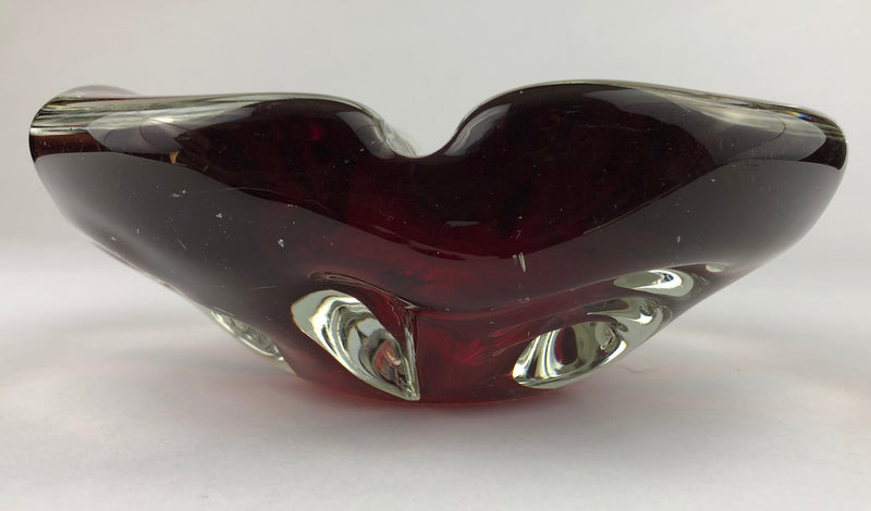 Low side view of a ruby-red Murano sommerso cigar ashtray, showing the curved rim and clear glass detailing around the base.