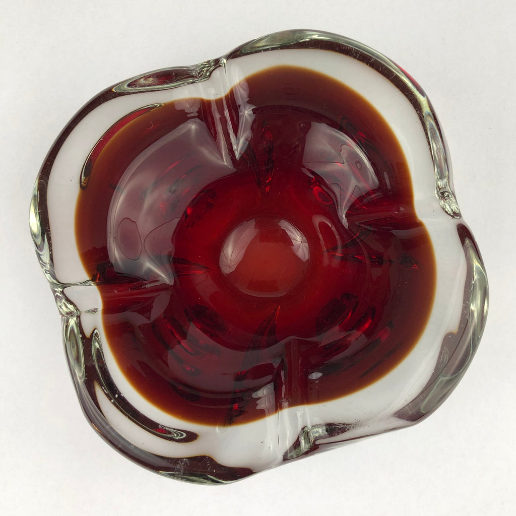 Vintage Murano sommerso ruby-red glass cigar ashtray viewed from above, showing its four-lobed shape and clear glass rim.
