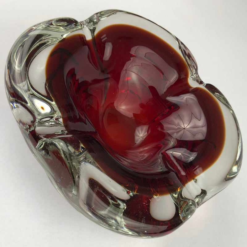 Vintage Murano glass cigar ashtray with a deep ruby-red bowl encased in thick clear glass, viewed at an angle.
