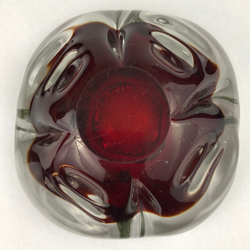 Underside of a vintage Murano ruby-red glass ashtray, showing its circular base and light surface scratches.