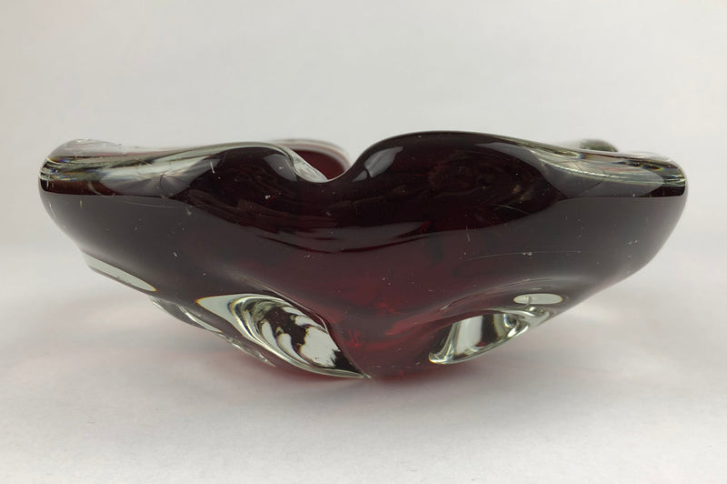Side profile of a vintage Murano sommerso ashtray, showing its dark ruby-red core and sculptural clear glass base.