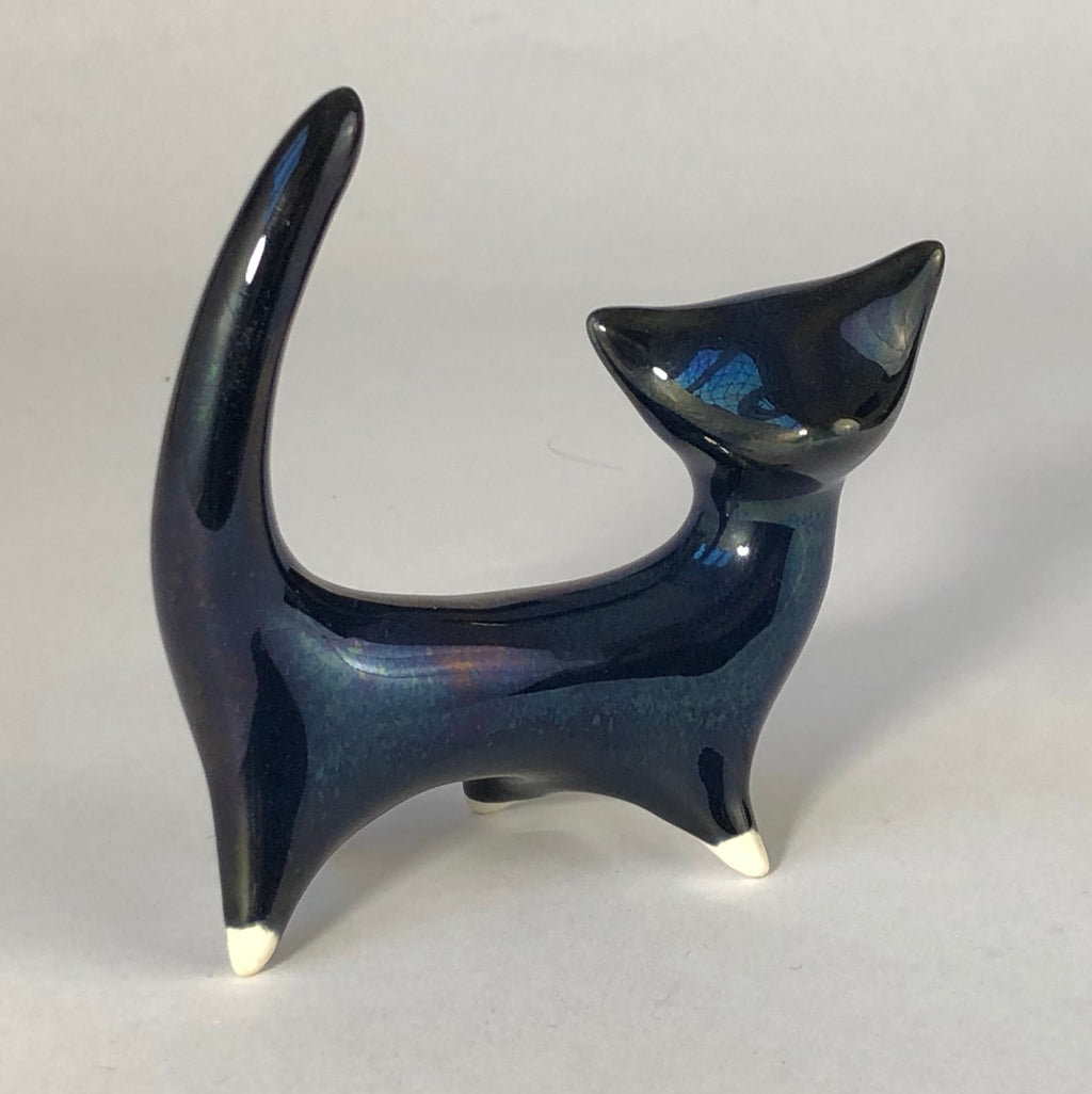 Side view facing right: Mid-century ceramic cat with midnight-blue lustre glaze, a tall curved tail, pointed ears and cream-tipped feet.