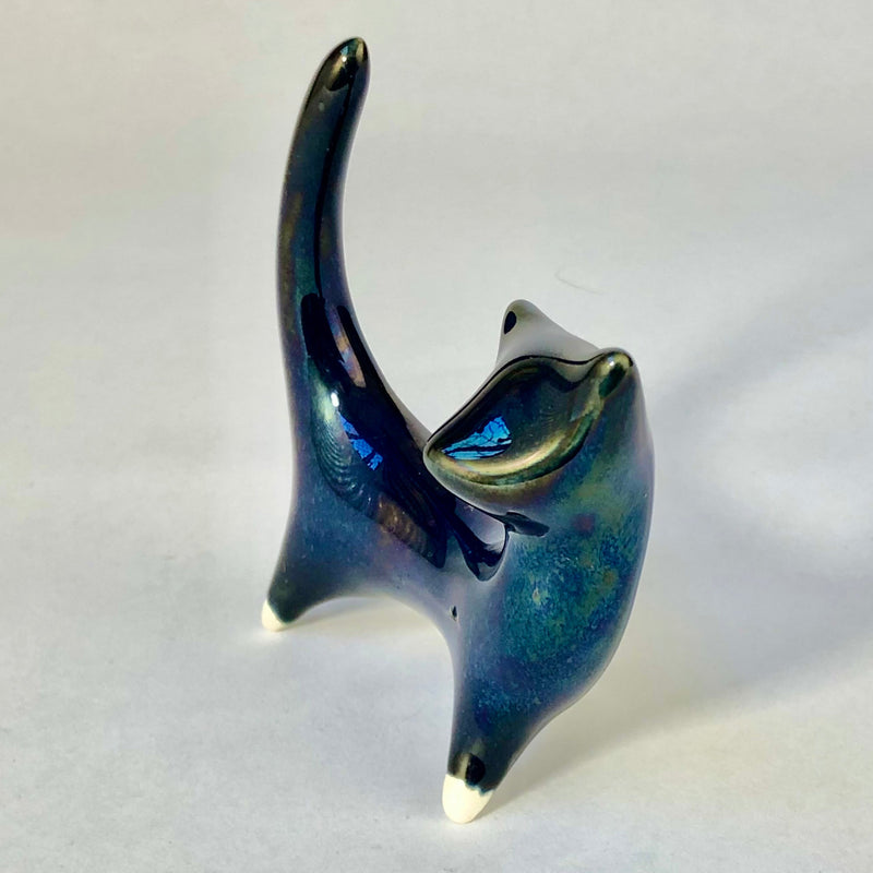 Close angled view of the ceramic cat showing its pointed ears, curved neck and iridescent midnight-blue glaze.