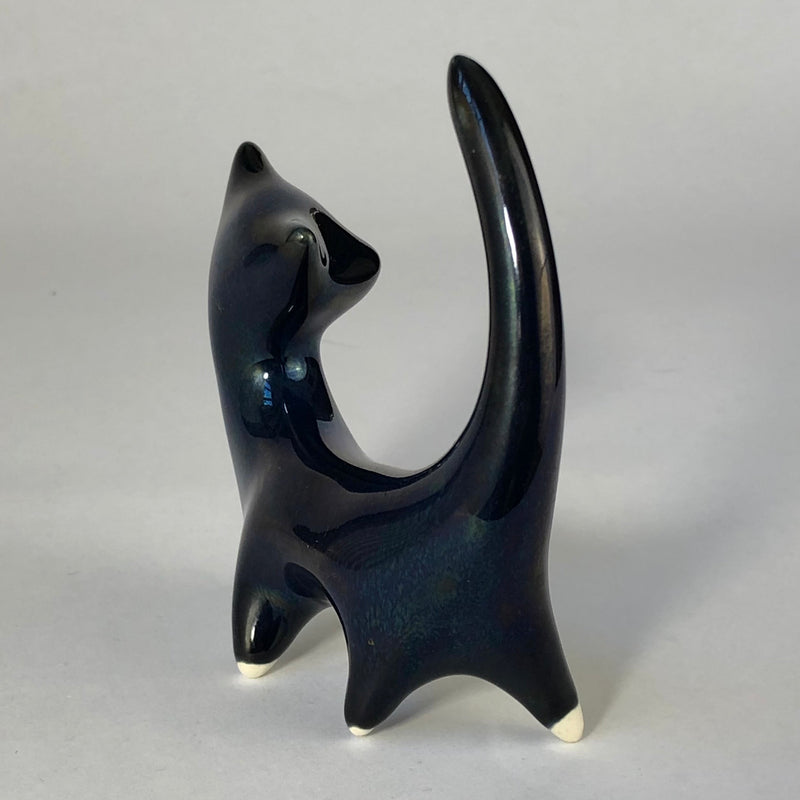 Rear view of the ceramic cat with a sweeping upright tail and green and violet reflections in the blue lustre glaze.