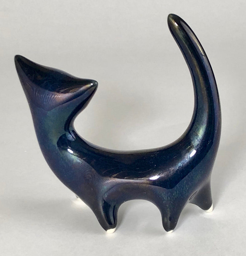 Full side view of the ceramic cat facing left, with blue-green lustre reflections, an arched body and cream-tipped feet.