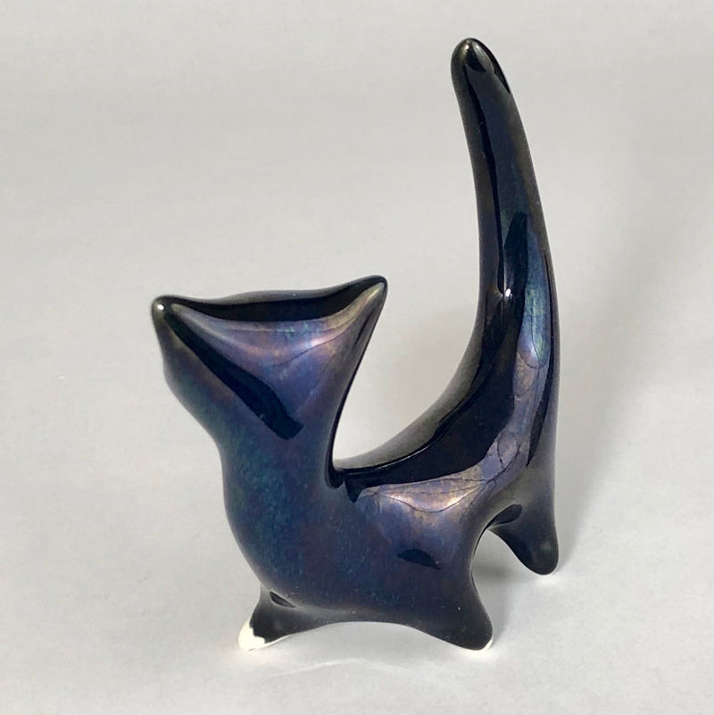 Three-quarter view of the back of  blue ceramic cat showing its broad triangular head, elongated body and tall curved tail.