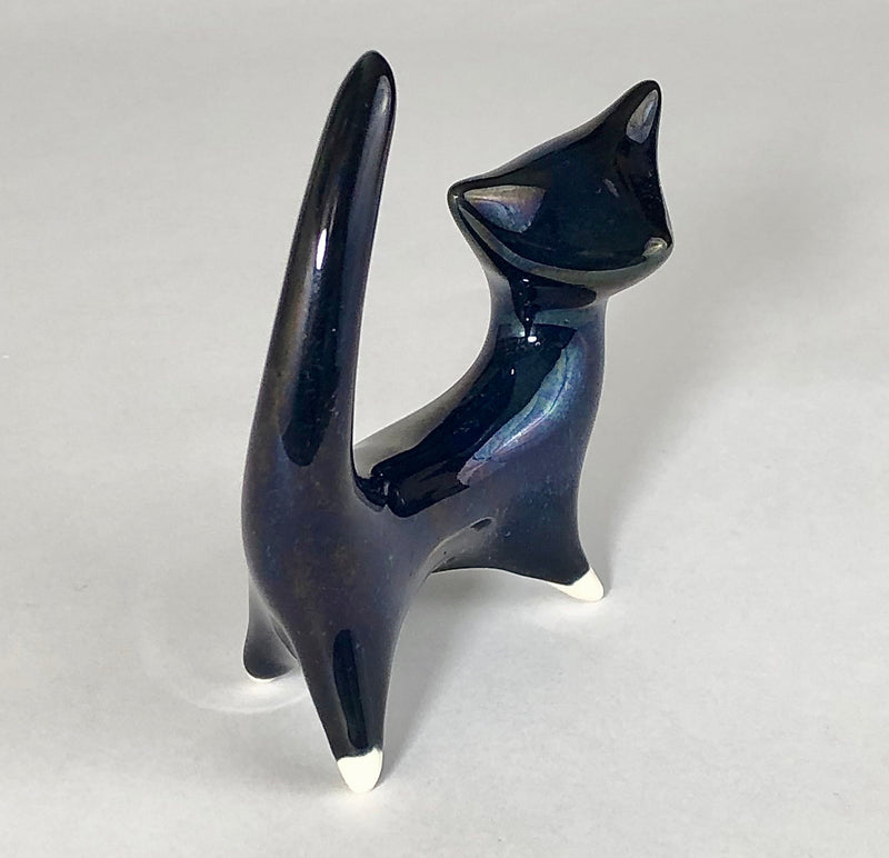 Angled view of the midnight-blue ceramic cat showing its upright tail, slender body and cream-tipped paws.
