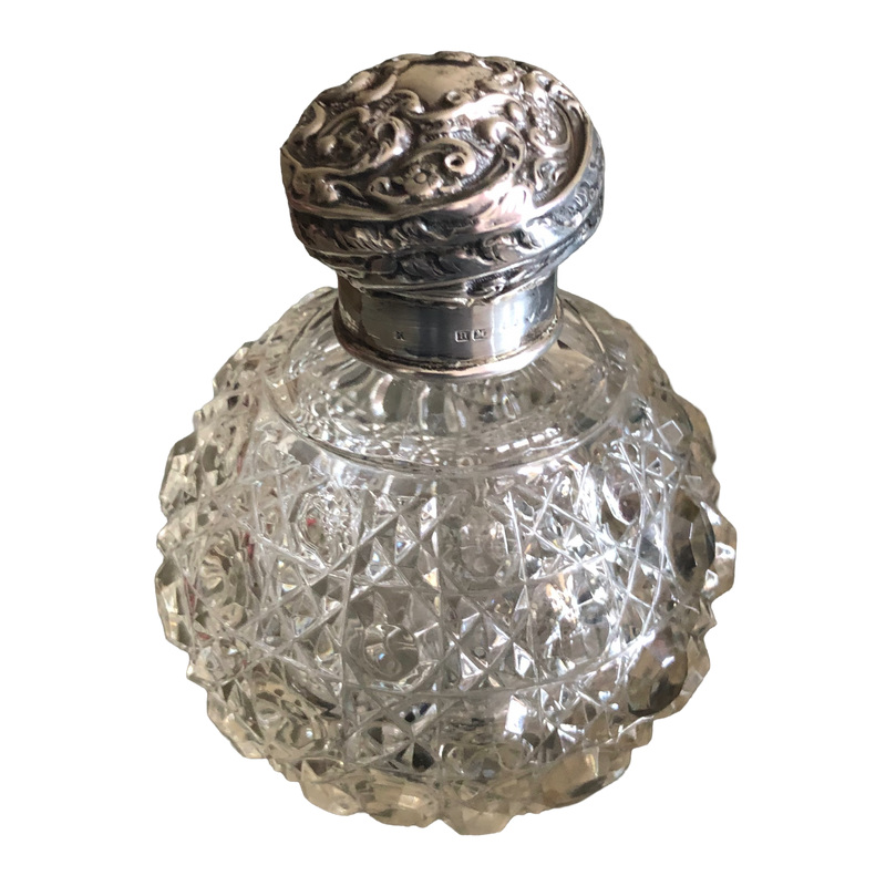 Victorian silver and cut-glass scent bottle showing the floral embossed lid and hallmarks on the silver collar.
