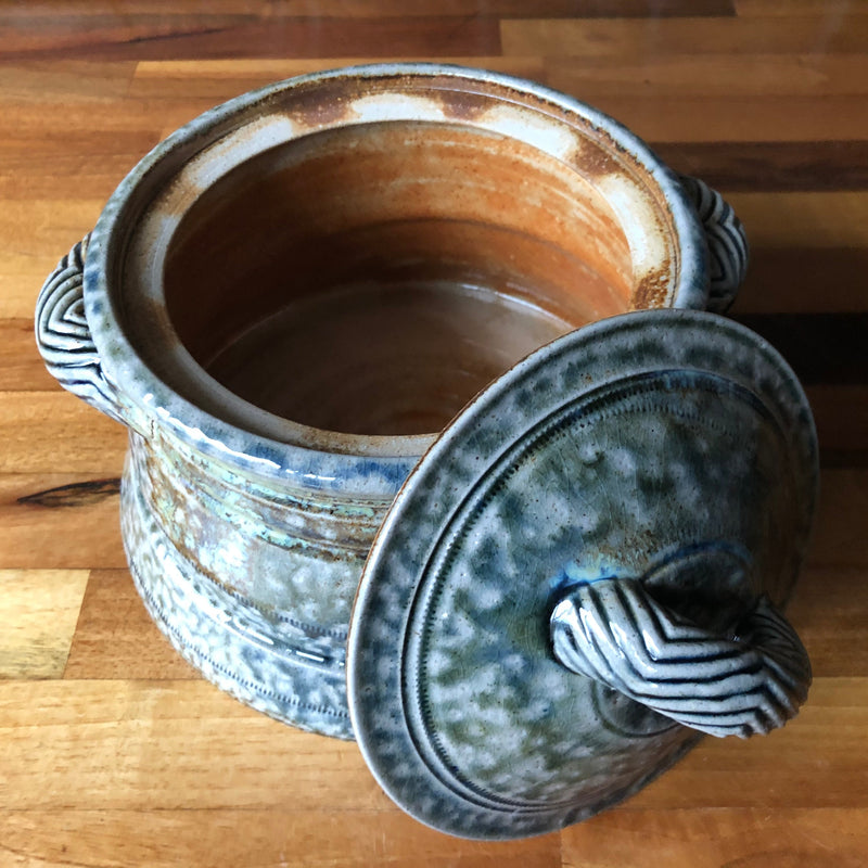  Open Jane Hamlyn stoneware casserole showing the warm brown interior, with the blue-grey lid resting against the front.