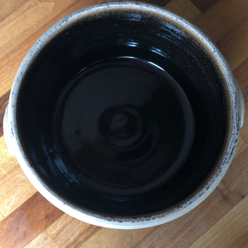 Overhead view inside Alan Brough stoneware casserole showing the glossy dark brown glaze and circular throwing lines.