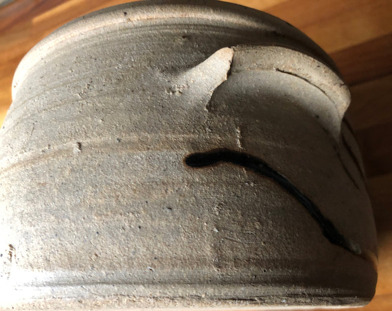 Detail of Alan Brough casserole showing a small applied side handle, textured buff stoneware and dark glaze trail.