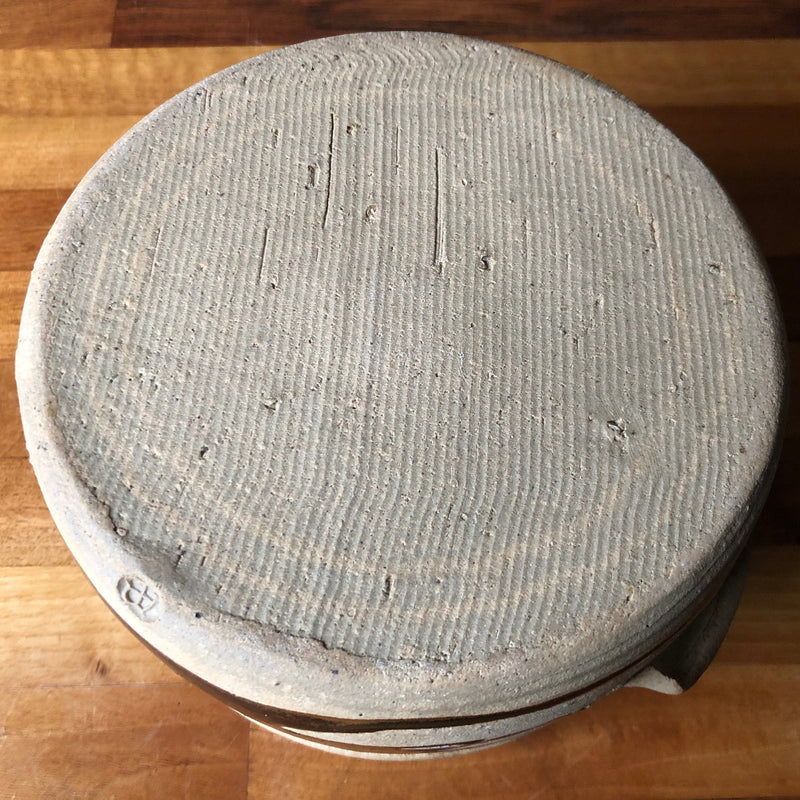 Underside of Alan Brough stoneware casserole showing the unglazed textured base and impressed AB mark at the edge.
