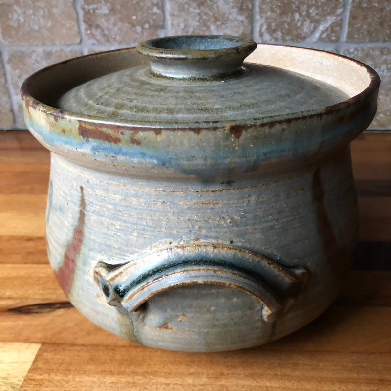 Side view of Vera Tollow lidded casserole showing an arched handle with a blue-green glazed groove.