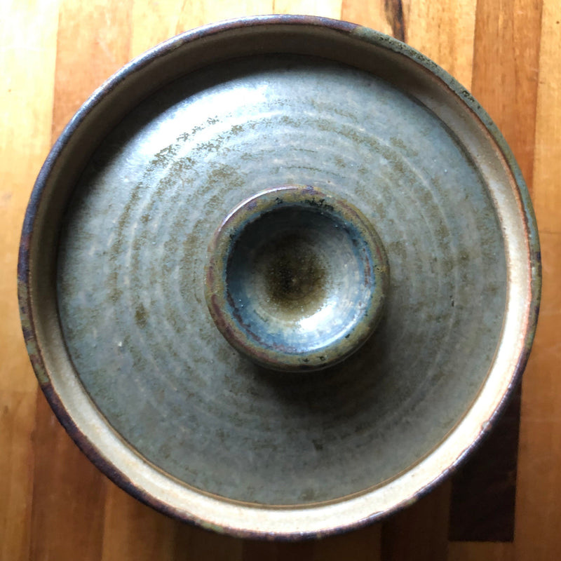 Overhead view of Vera Tollow casserole lid showing its central hollow knob and concentric rings in the olive-grey glaze.