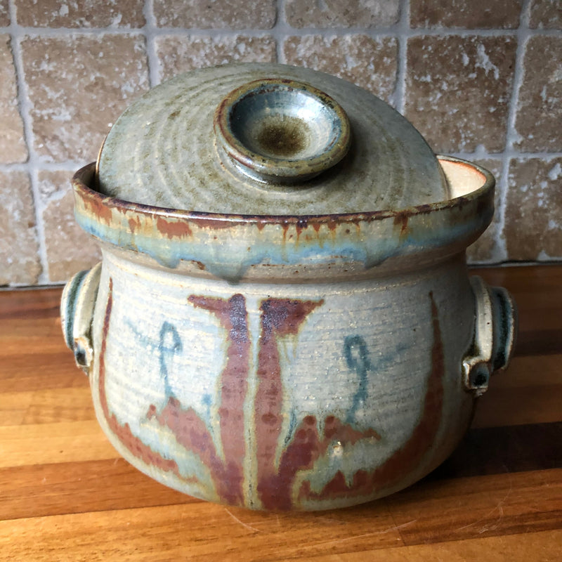Vera Tollow studio pottery casserole with lid tilted to show its deep, bowl-shaped knob and concentric throwing rings.