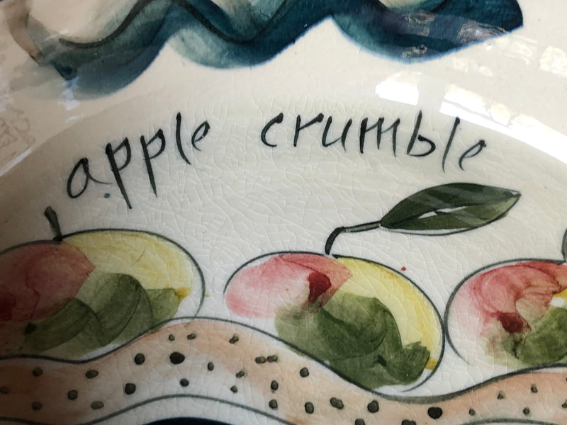 Close-up of hand-painted apples and apple crumble lettering inside the cream-glazed pottery dish.