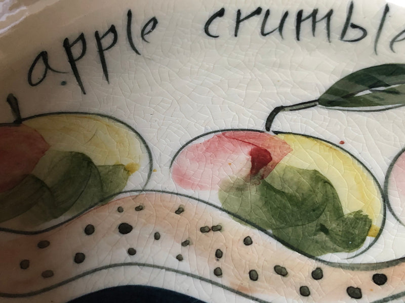 Detail of the apple crumble dish interior showing loose hand-painted fruit decoration and lettering.