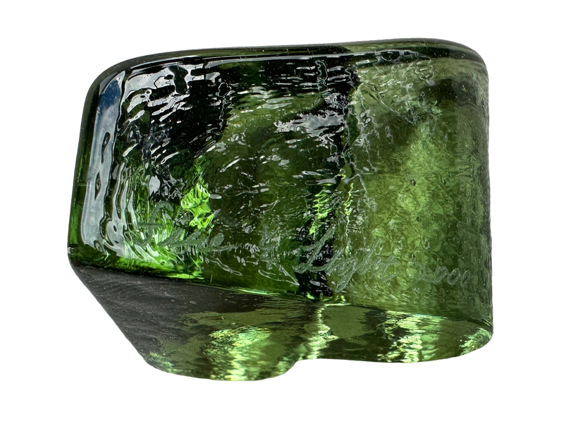 Low side view of the Fire & Light green glass heart paperweight showing its thick profile , signature, and uneven surface texture.
