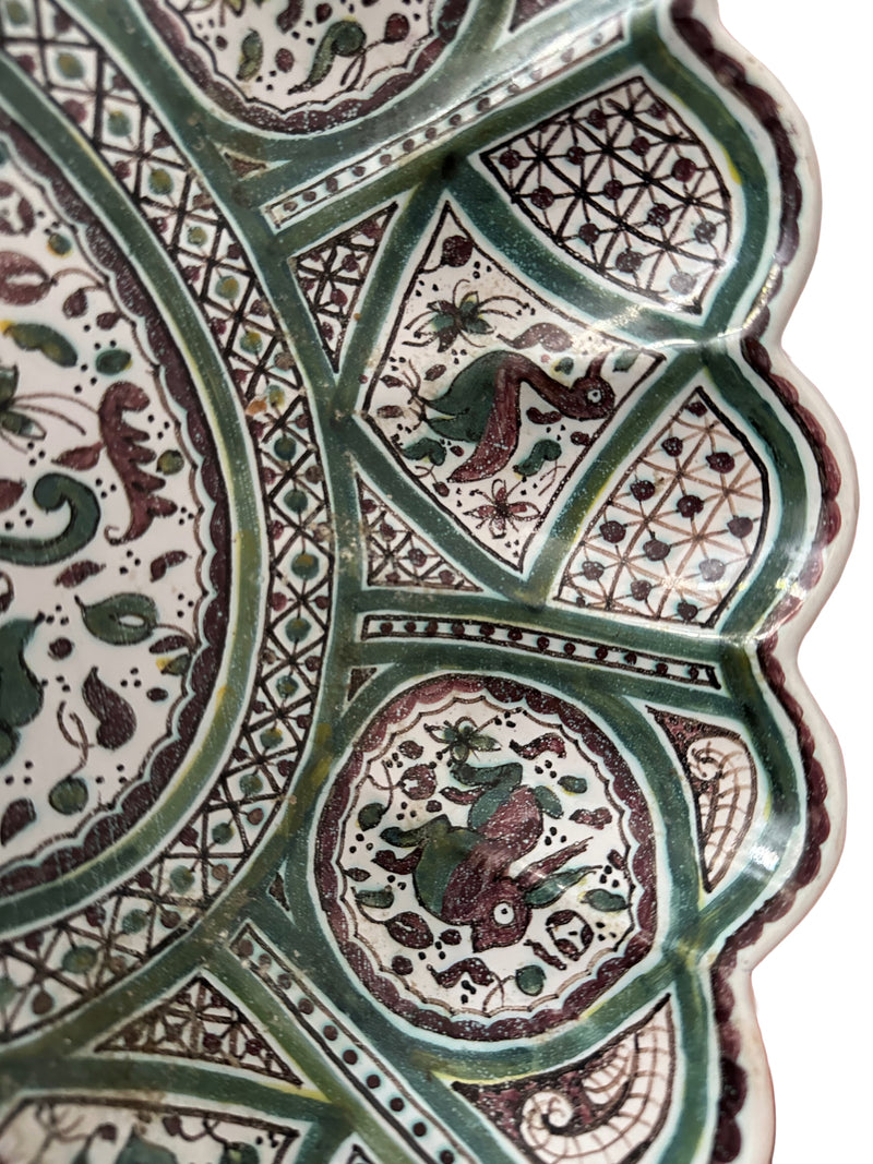 Close-up detail, upper right quadrant (interior)c lose-up of Portuguese Coimbra faience bowl interior showing hand-painted fantastical bird and rabbit motifs in green and manganese, geometric lattice panels