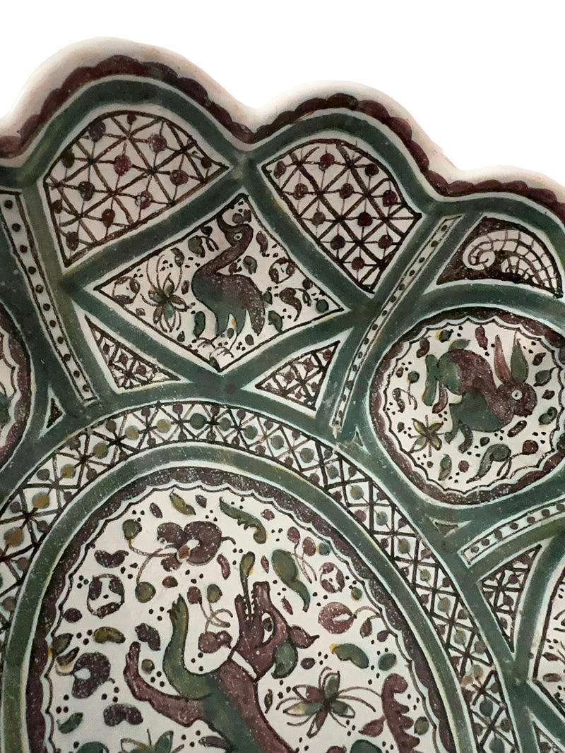  Close-up detail, upper left quadrant (interior)Detail of Coimbra faience bowl interior with hand-painted peacock and hare motifs, green geometric trellis and floral medallion panels, scalloped rim edge